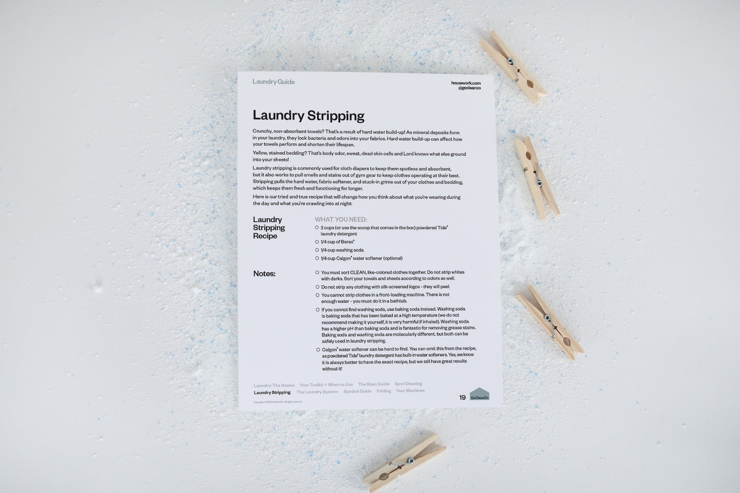 A laundry guide showing laundry stripping instructions is displayed with clothes pins and spilled laundry powder.