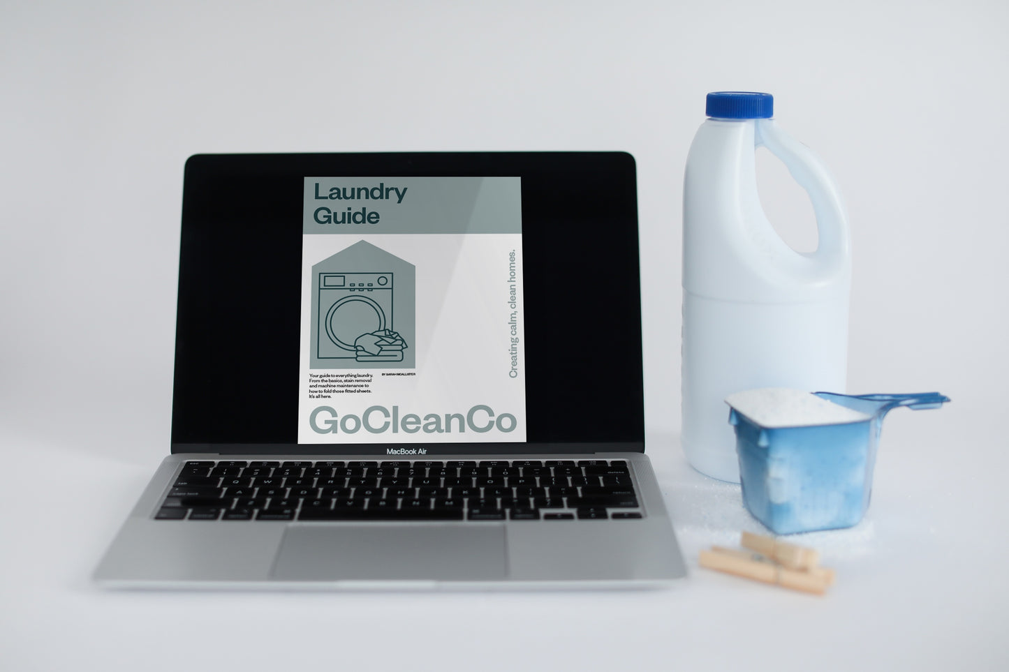 GoCleanCo Laundry Guide is displayed on a laptop next to a bleach bottle and laundry detergent.