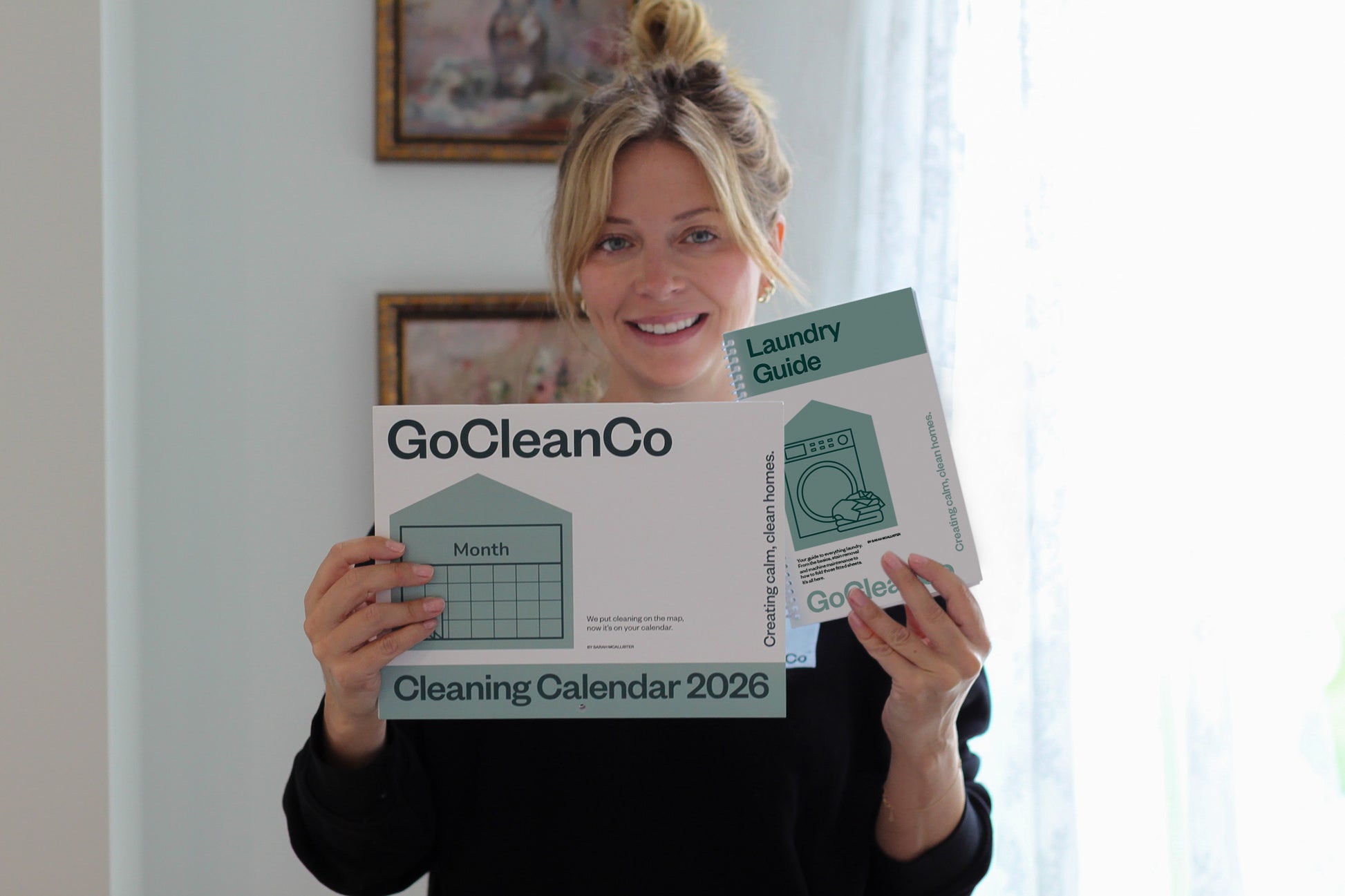 Woman holding a GoCleanCo cleaning calendar 2026 and laundry guide in a home setting