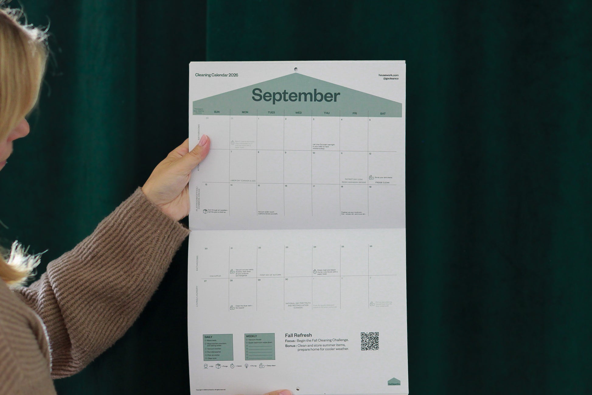 Person holding a large calendar sheet with September 2025 on a dark green background