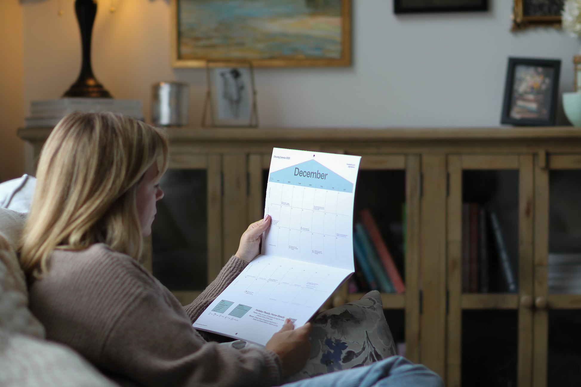 Woman sitting on a couch holding a calendar in a living room.