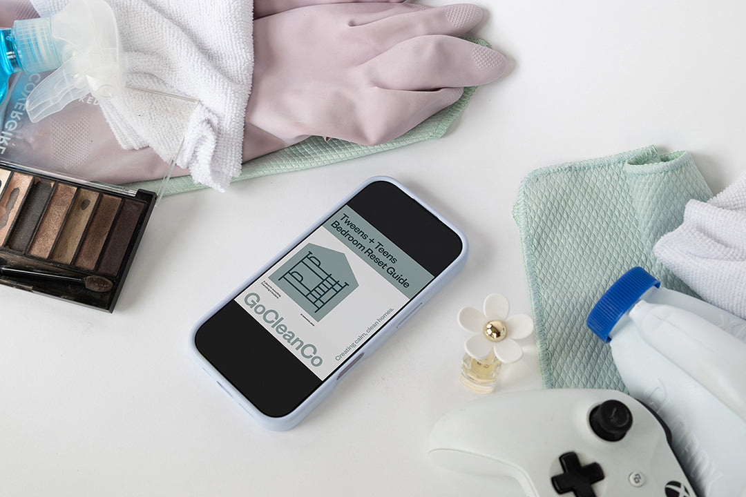 Smartphone displaying Tweens + Teens Bedroom Reset Guide on a white surface with cleaning supplies.