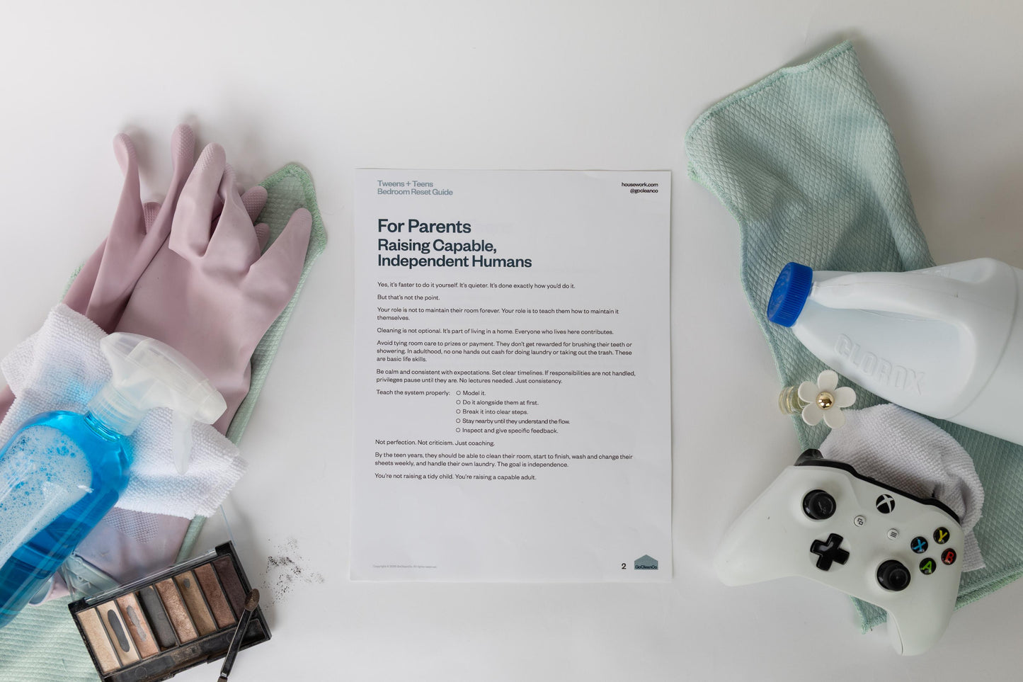 Cleaning supplies, makeup and a gaming controller on a white surface with a document 'For Parents Raising Capable Independent Humans'.