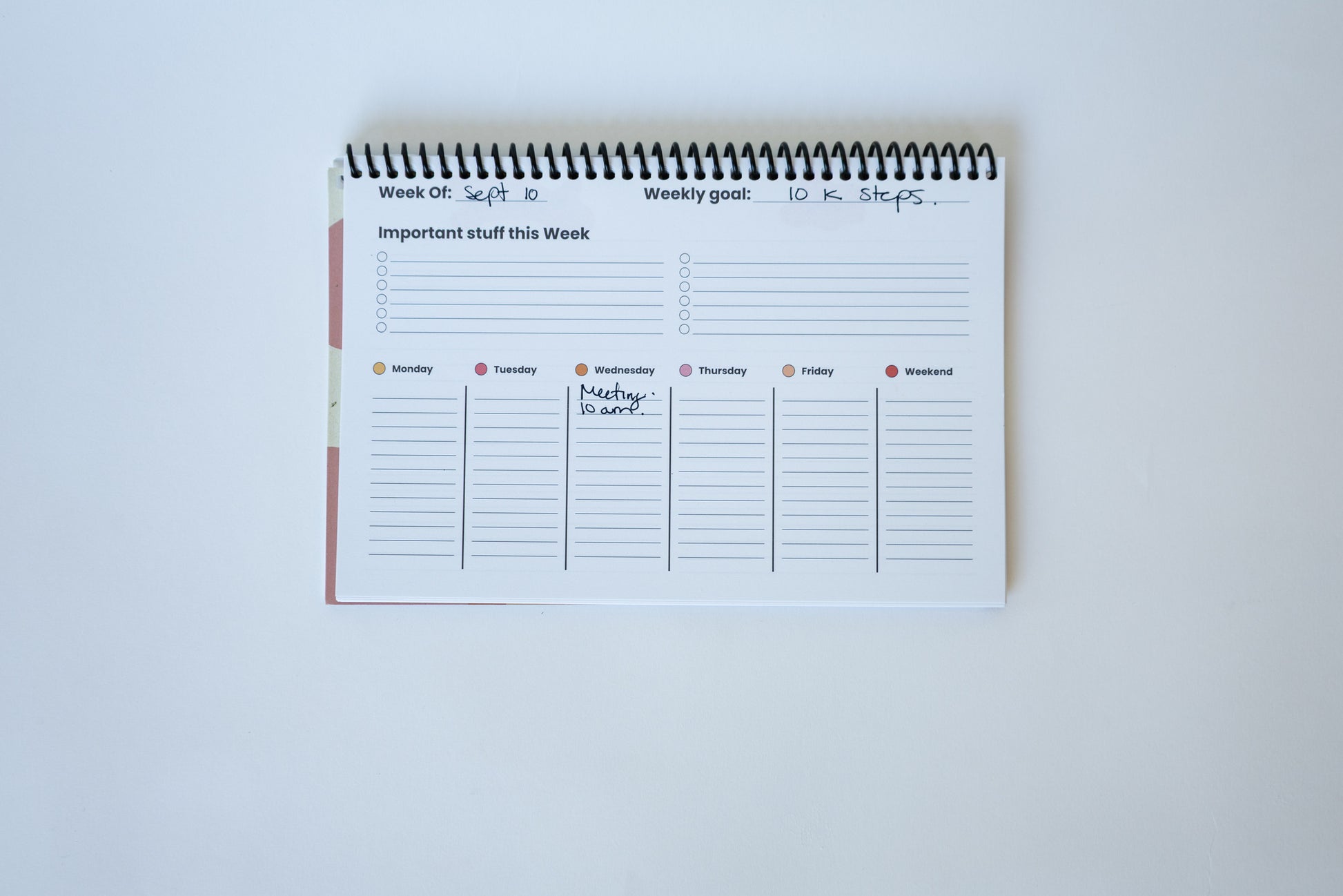 A spiral-bound weekly planner pad with lined sections for daily planning, shown open on a plain white background.
